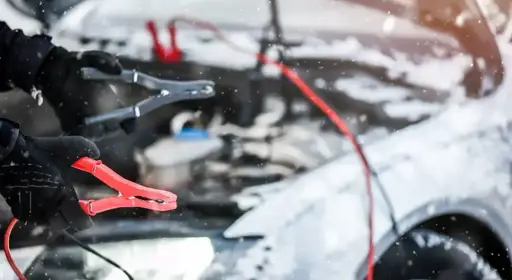 Wie kann ich mein Auto richtig überbrücken? Eine behandschuhte Hand hält ein Überbrückungskabel.