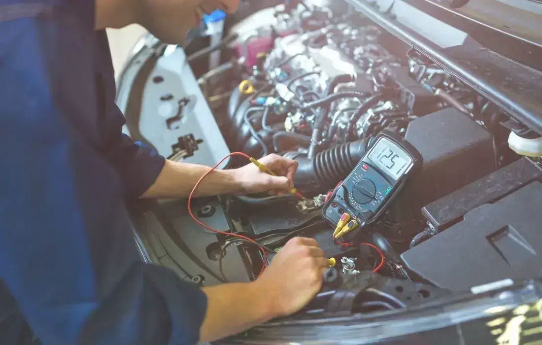 Die Grafik zeigt einen Autobatterie-Test in einer Werkstatt mit einem Multimeter.