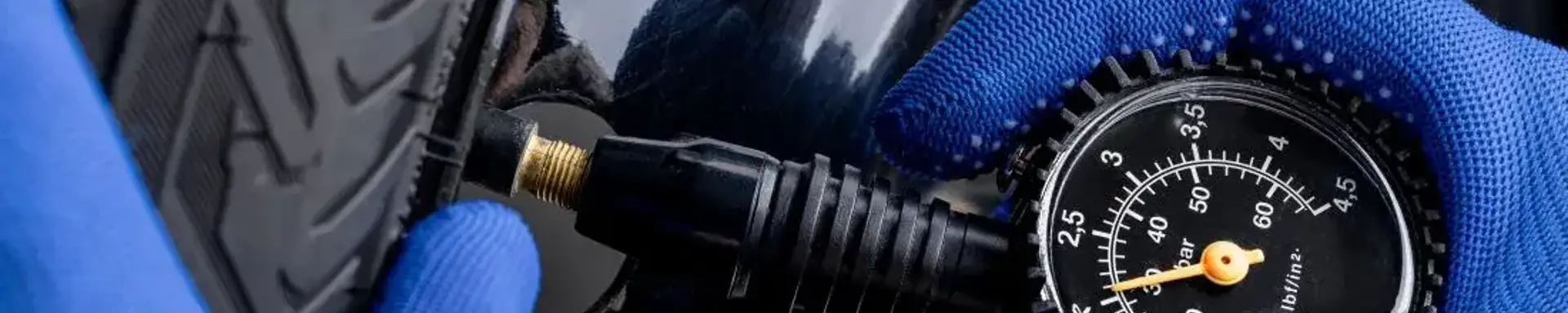 Wie lässt sich der Reifendruck beim Auto prüfen? Die Grafik zeigt zwei Hände mit blauen Handschuhen, die den Reifendruck am Auto prüfen.