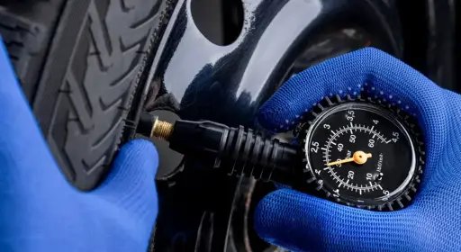 Wie lässt sich der Reifendruck beim Auto prüfen? Die Grafik zeigt zwei Hände mit blauen Handschuhen, die den Reifendruck am Auto prüfen.