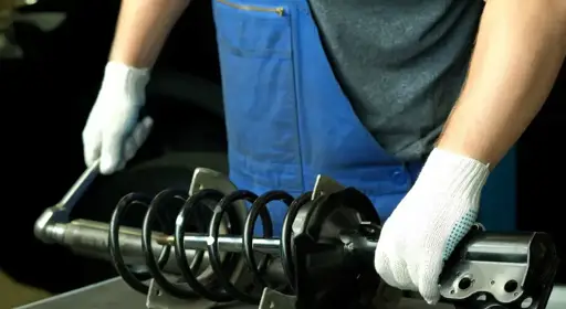 Was wird bei einer Stoßdämpfer-Reparatur gemacht? Ein Stoßdämpfer wird im Zuge einer Reparatur von einer Person inspiziert.