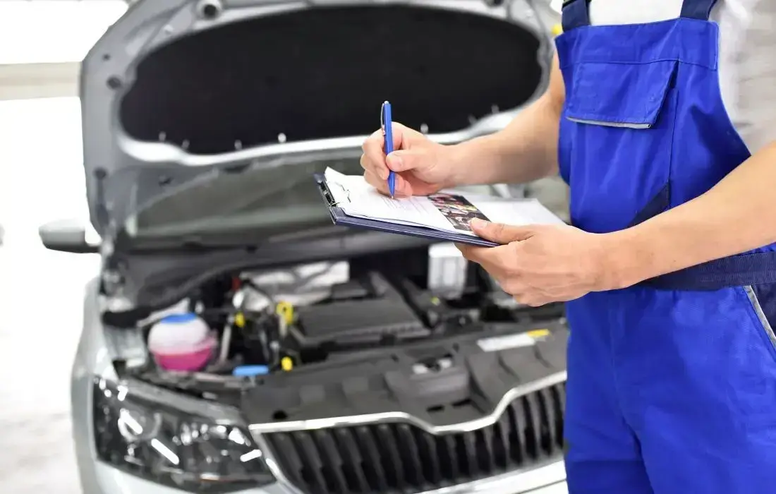Die Grafik zeigt einen Prüfer bei der Hauptuntersuchung eines Autos, der die Checkliste für die HU-Plakette durchgeht.