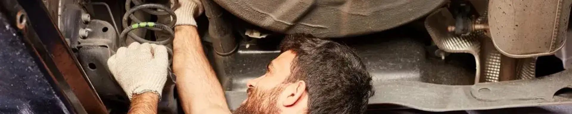 Welche Lebensdauer haben Stossdaempfer? Das Bild zeigt einen Mann, welcher an einem Auto den Stossdaempfer mit einer begrenzten Lebensdauer inspiziert.