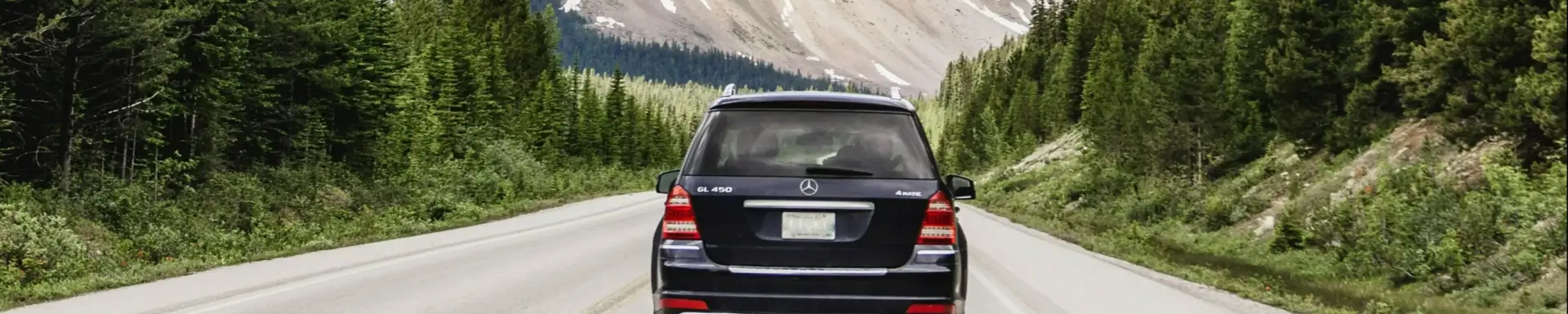 Welche Folgen hat das Fahren von Winterreifen im Sommer? Ein Auto bei sommerlichem Wetter mit verschneiten Bergen im Hintergrund, was den winterlichen Aspekt symbolisiert.