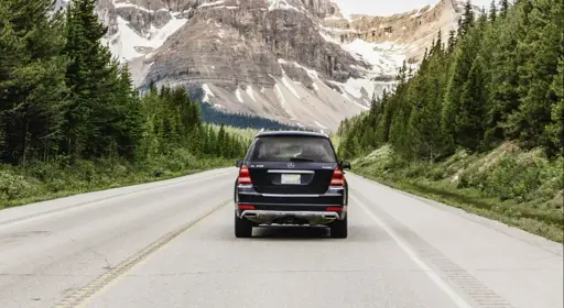 Welche Folgen hat das Fahren von Winterreifen im Sommer? Ein Auto bei sommerlichem Wetter mit verschneiten Bergen im Hintergrund, was den winterlichen Aspekt symbolisiert.