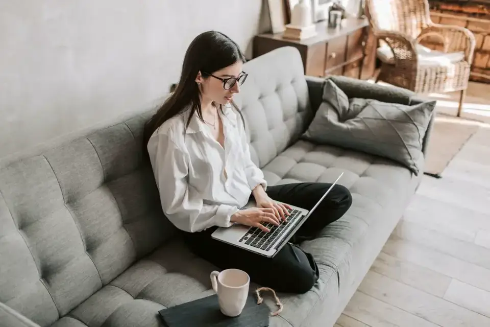 Eine Frau, die auf der Couch am Laptop sitzt, informiert sich über die Winterreifenpflicht in Deutschland.